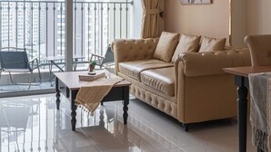 Un salon moderne avec un canapé beige, une table basse et un lustre. Une grande fenêtre offre une vue sur de hauts immeubles.