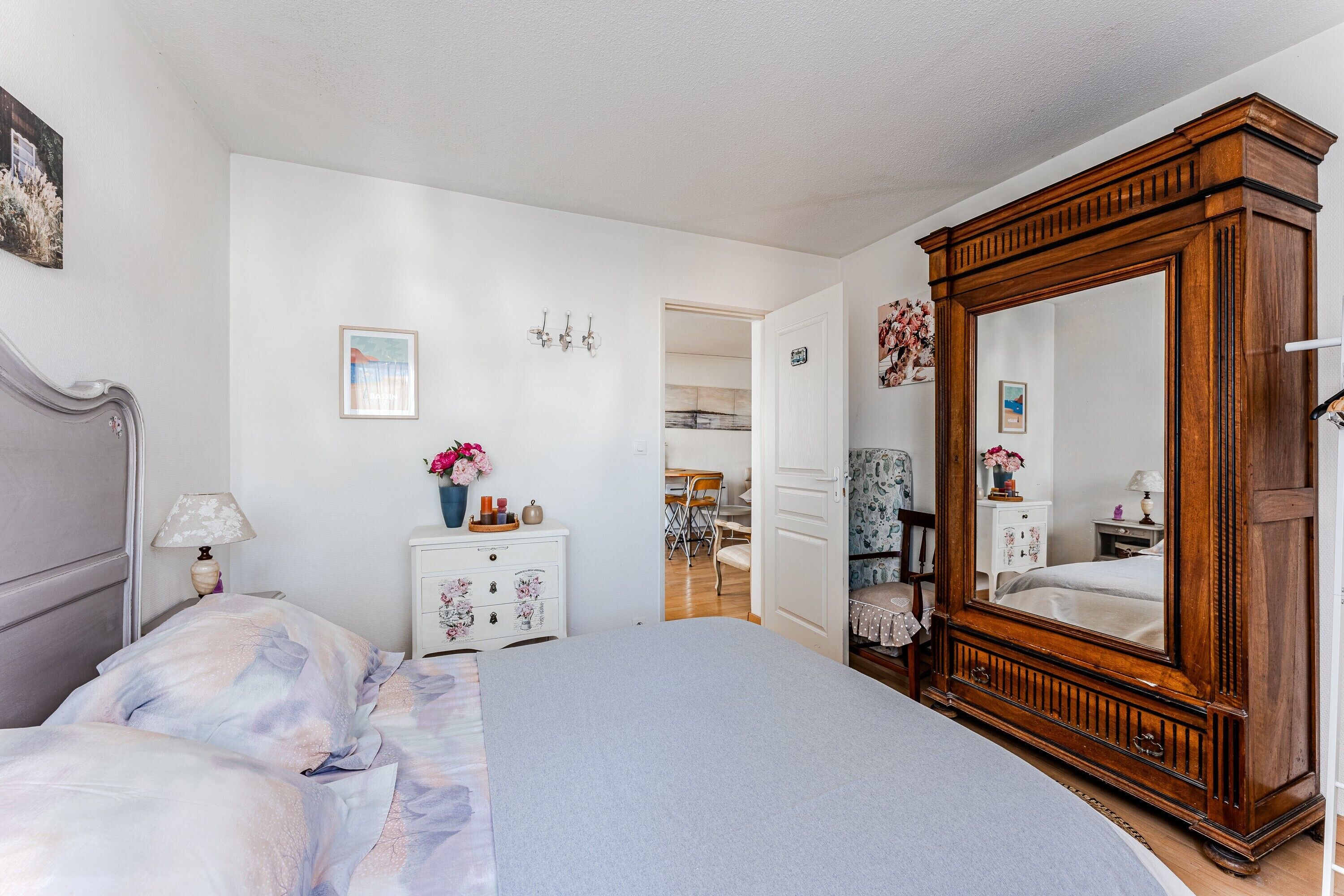 Une chambre à coucher avec un grand lit, une commode, un miroir et une porte donnant sur une autre pièce.