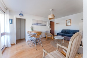 Un salon comprenant un canapé, une table à manger avec des chaises, une petite table ronde, un luminaire suspendu et une porte.