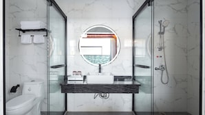 A modern bathroom with a glass shower enclosure, a white toilet, a marble-tiled wall, a round mirror, and a black countertop. - Sanya Anyun  Coastal Lodge (Sanya)