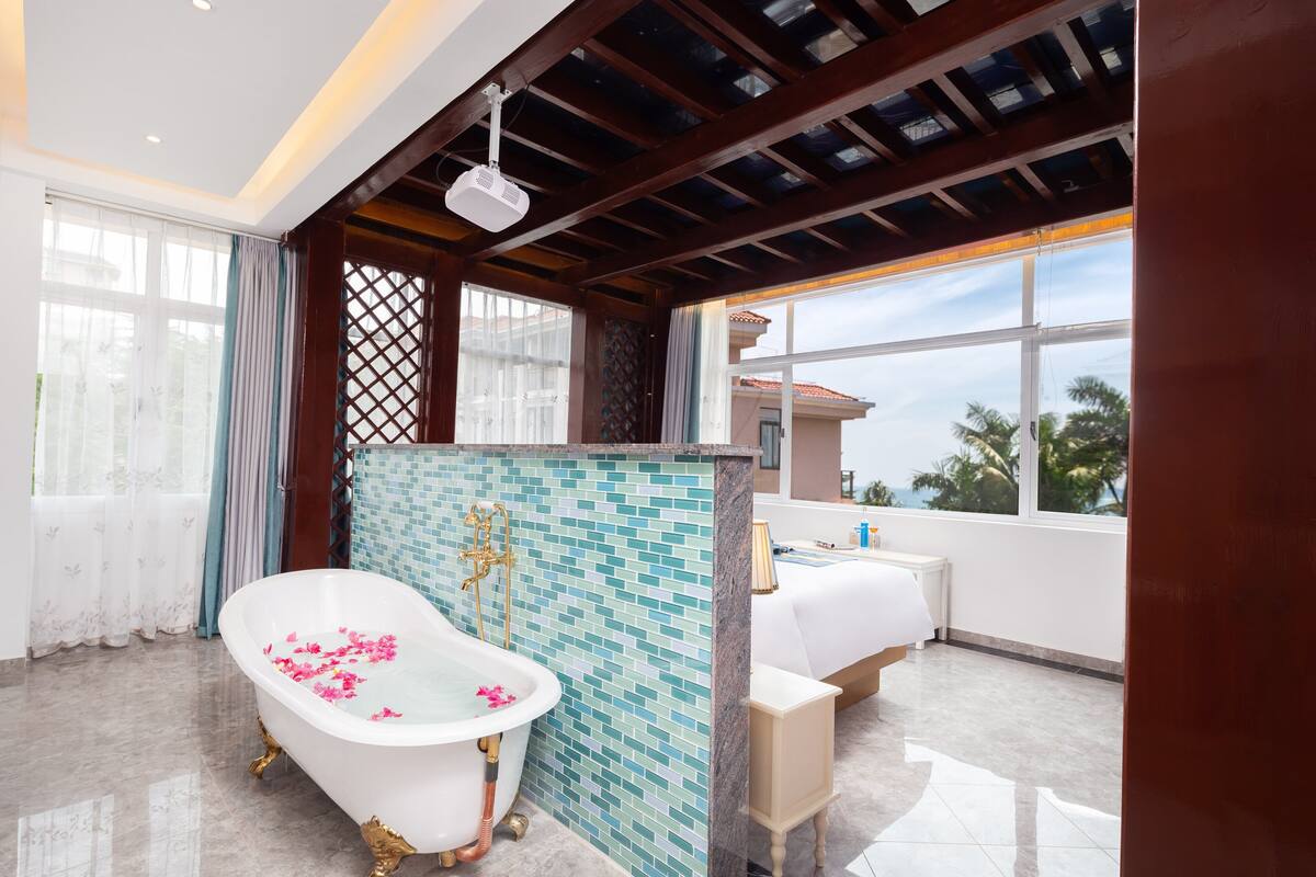 Une salle de bain avec une baignoire sur pieds, un espace de douche carrelé et une fenêtre donnant sur des palmiers.