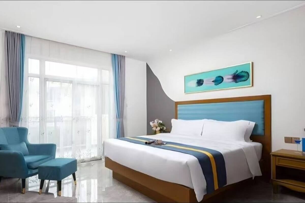Une chambre d’hôtel avec un lit, une chaise, une table de chevet, une fenêtre avec des rideaux et un tableau au mur.