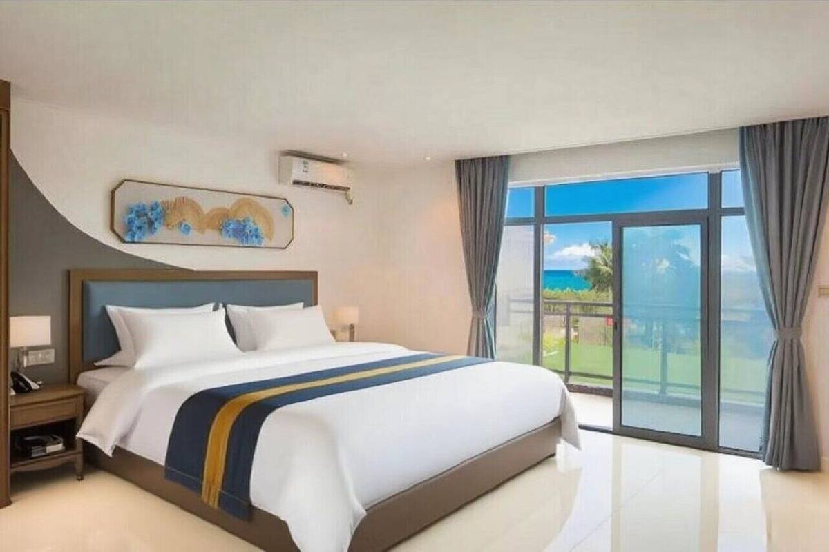 Une chambre d’hôtel avec un grand lit, une table de chevet, un tableau au mur et une vue sur l’extérieur grâce à une grande fenêtre.