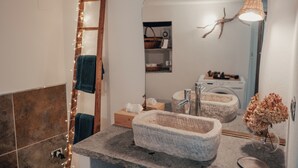 Ein Badezimmer mit einem Steinkonstruktion als Waschbecken, einer Holzleiter, einem Handtuchhalter, einem Spiegel und einer hängenden Leuchte.
