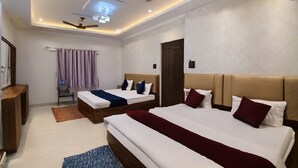 Una habitación de hotel moderna con dos camas, ventilador de techo, iluminación empotrada y una pequeña zona de estar con una mesa y sillas.