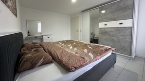 A modern bedroom with a large bed, a wardrobe with a marble finish, and a bedside table with a mirror. - Stylish apartment in a modern ambience in Tuttlingen (Tuttlingen)