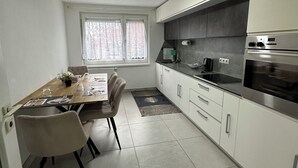 A modern kitchen with white cabinets, a dining table with chairs, and a built-in oven. - Stylish apartment in a modern ambience in Tuttlingen (Tuttlingen)