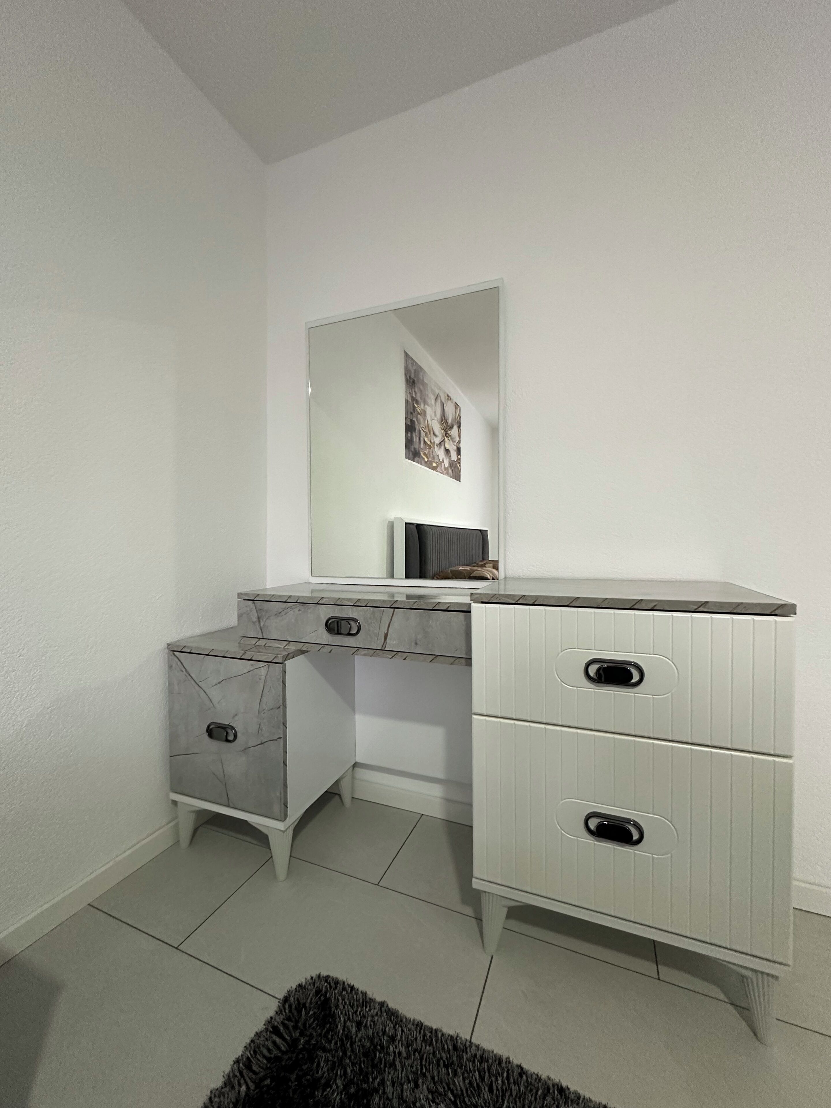 Une chambre à coucher moderne avec une commode blanche, un miroir et une petite œuvre d’art accrochée au mur.