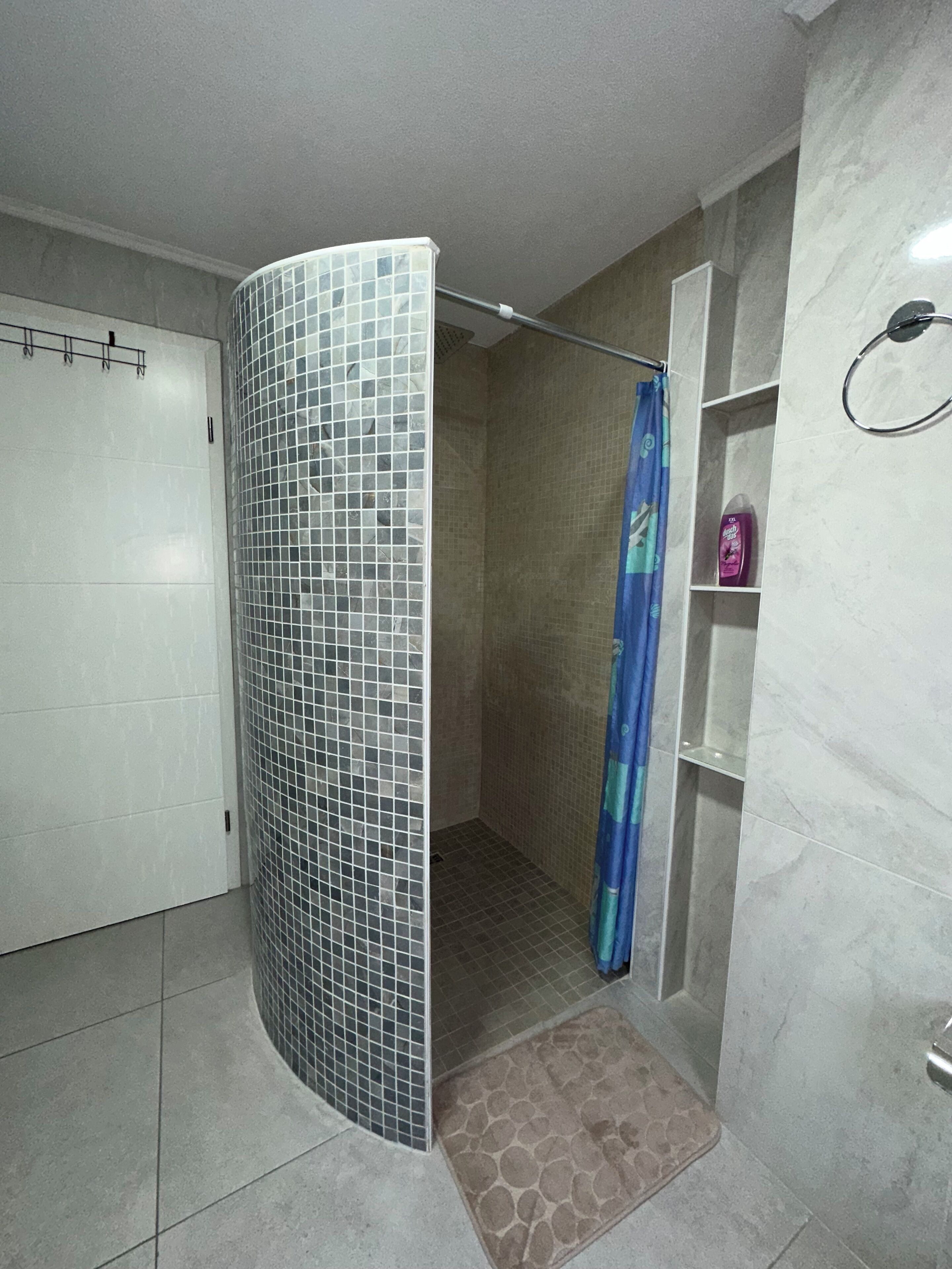 A shower area with a tiled wall, a shower curtain, and a tiled floor.