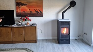 Una sala de estar con una estufa de leña, un cuadro de jirafas, un aparador de madera y un televisor.