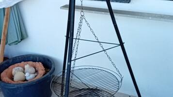 A metal hanging basket with a chain, placed on a tiled floor next to a window with a metal grill.