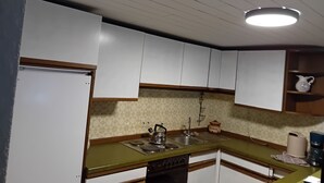 Una cocina con armarios blancos, encimera verde, estufa, fregadero y una lámpara en el techo.