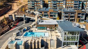 A modern building with multiple balconies, a swimming pool, and a ski lift in the background. - All-Season Escape | Ski-In/Out + Hot Tub + Clubhouse Amenities Canyons Village (Park City)