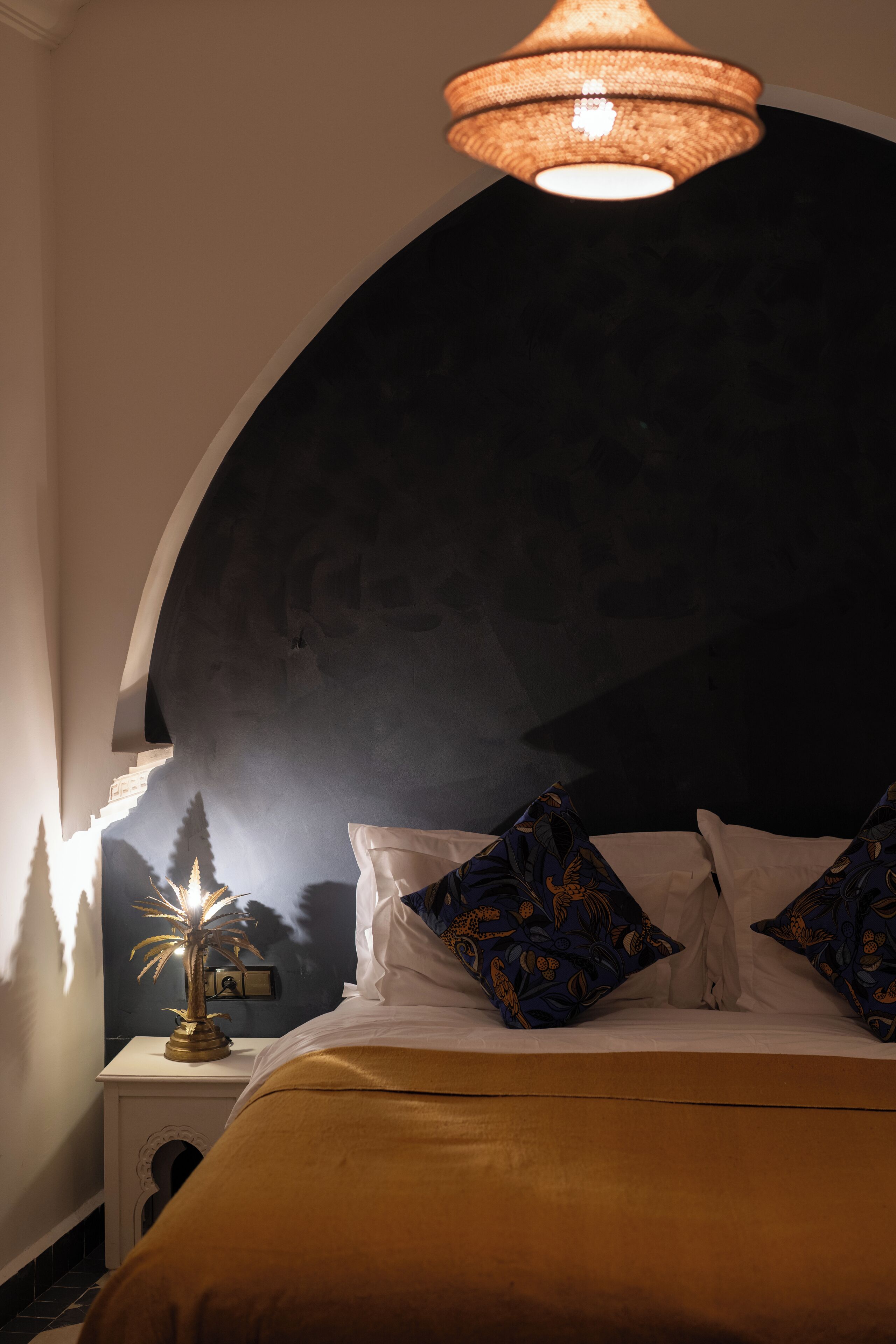 A bedroom with a bed, pillows, a nightstand, a lamp, and a wall with a decorative element.
