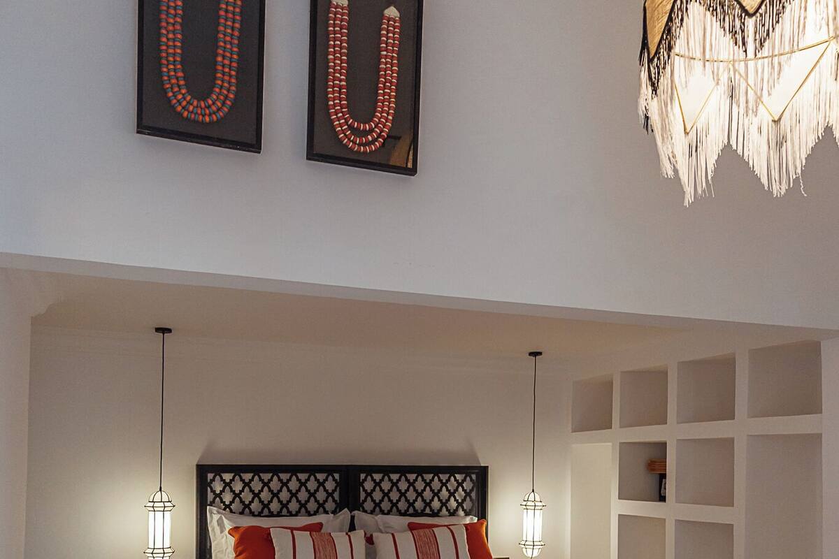 A bedroom with a bed, two wall-mounted light fixtures, a patterned rug, and a hanging light fixture.