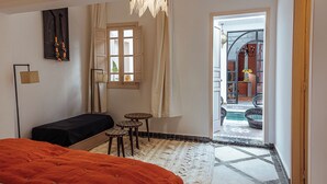 A bedroom with a bed, a bench, a small table, and a view of an outdoor area with a pool. - Riad le terra cotta (Marrakech)