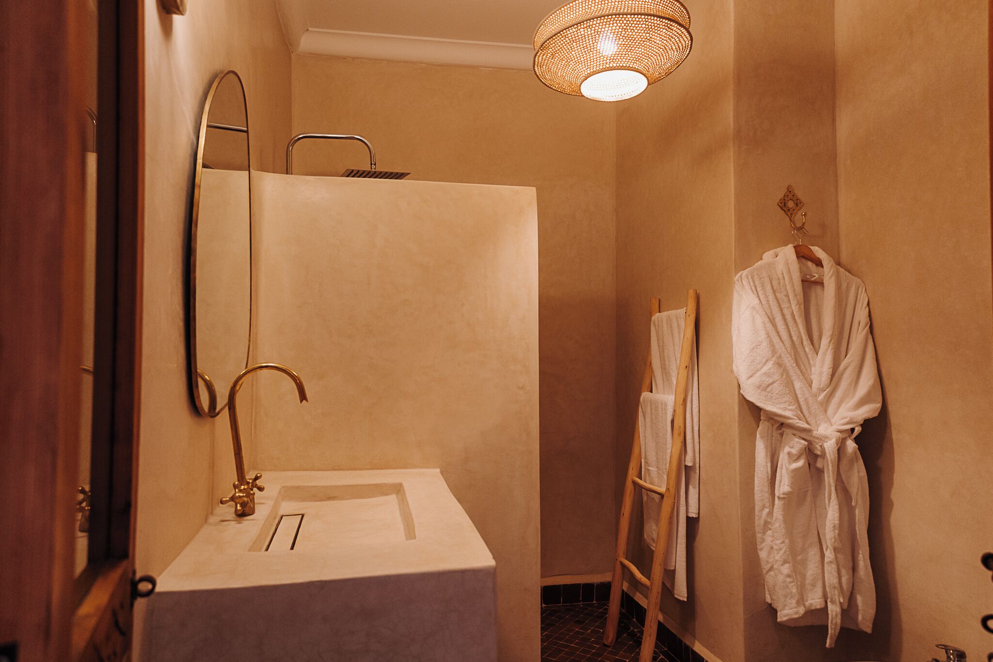 A bathroom with a sink, mirror, shower, and a robe hanging on the wall.