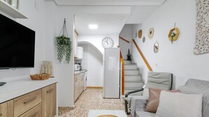 Ett modernt vardagsrum med en platt-TV, en soffa, ett soffbord och ett köksområde i bakgrunden.