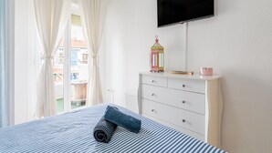 Ett sovrum med en säng, en byrå, en tv och ett fönster med gardiner.