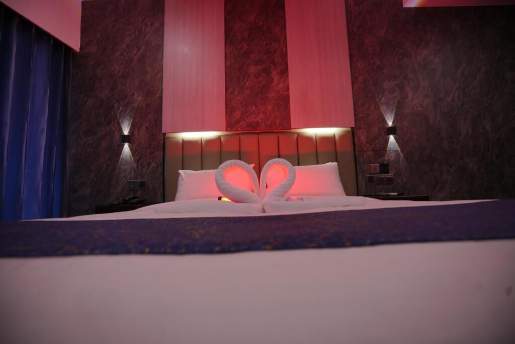 Una habitación de hotel con cama, cabecera con iluminación integrada y apliques de pared.