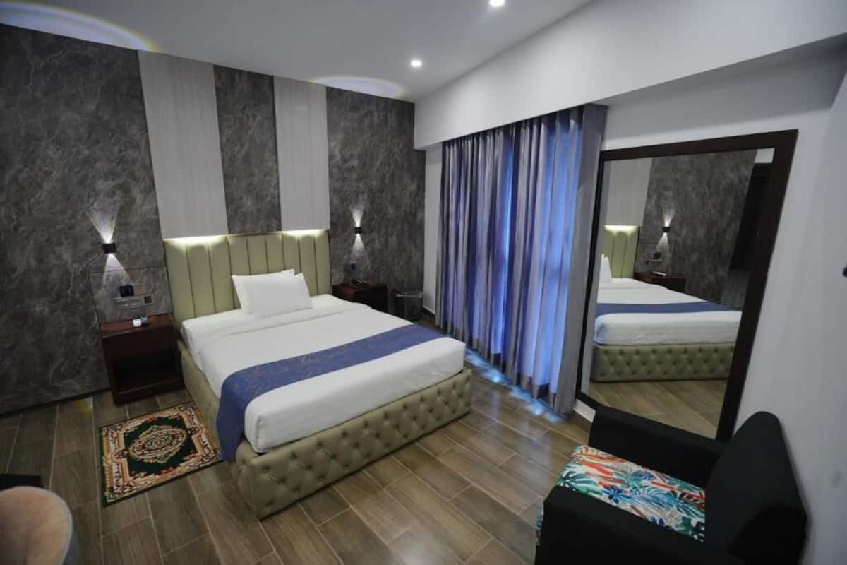 Une chambre d’hôtel moderne avec un grand lit, une table de chevet, un miroir et une chaise.