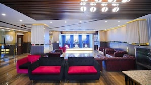 Una hall con una reception, area relax con divani rossi e neri, e un soffitto decorativo.