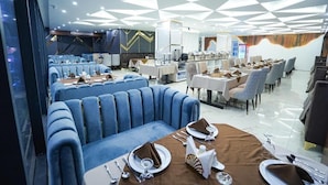 Un'area ristorazione moderna con sedute rivestite in blu, tavoli bianchi e un design geometrico del soffitto.