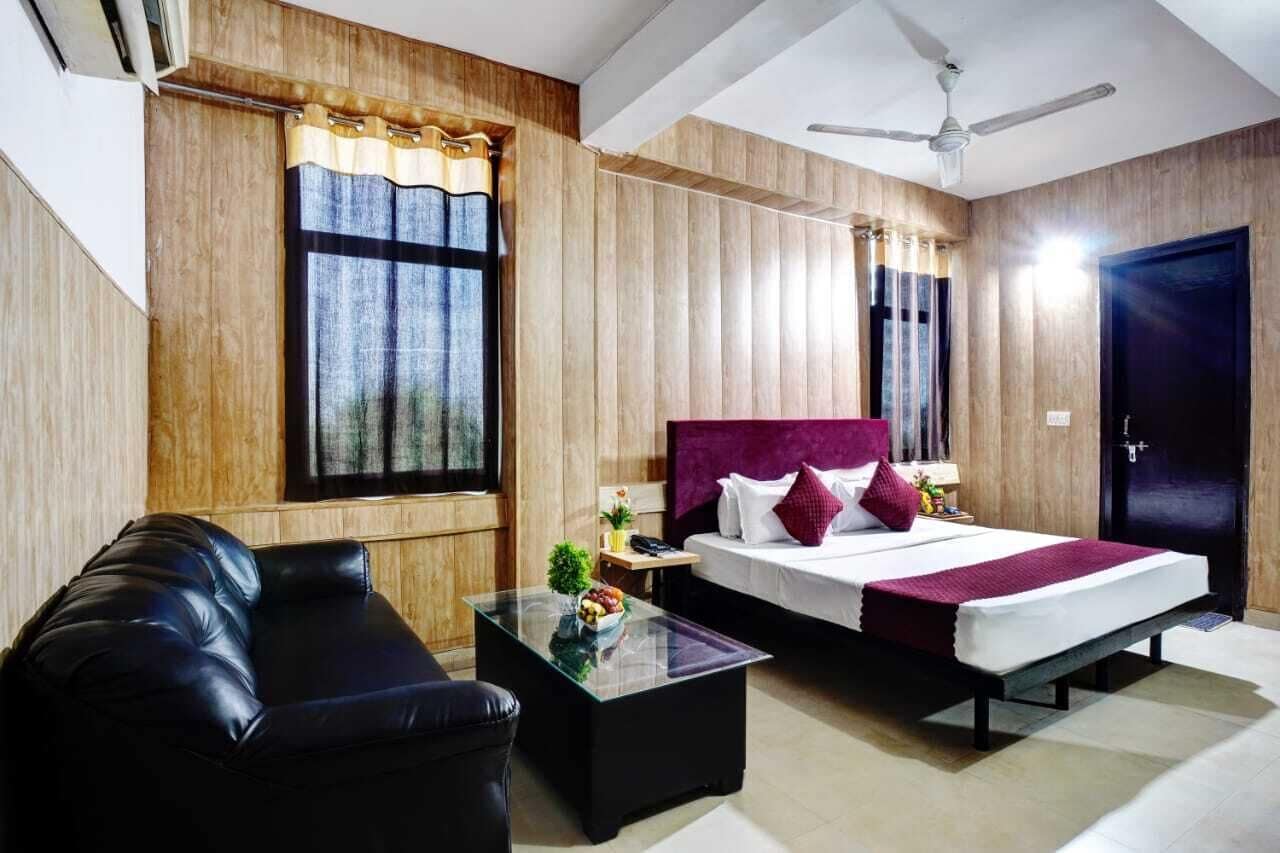 A hotel room with a bed, a sofa, a glass coffee table, and a ceiling fan.