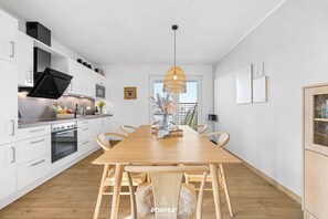 A modern kitchen with white cabinetry, a large wooden dining table, and a hanging light fixture.