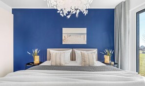 A bedroom with a bed, a chandelier, a painting, and a view of the outdoors.