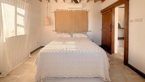 Ein Schlafzimmer mit einem Bett, einem Deckenventilator, Wandbehängen aus gewebtem Material und einer Holztür.