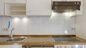 Una cucina con mobili bianchi, un lavello in acciaio inossidabile, forno a incasso e cappa aspirante.