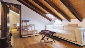 Een loft-achtige kamer met zichtbare houten balken, een witte bank, een houten salontafel en een boekenkast met boeken en dozen.