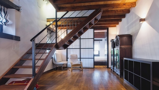 Een houten trap die leidt naar een vide met een comfortabele stoel en een kast.