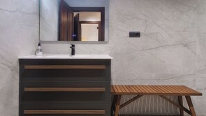 Een badkamer met een marmeren wand, een moderne wastafel met spiegel en een houten kruk.