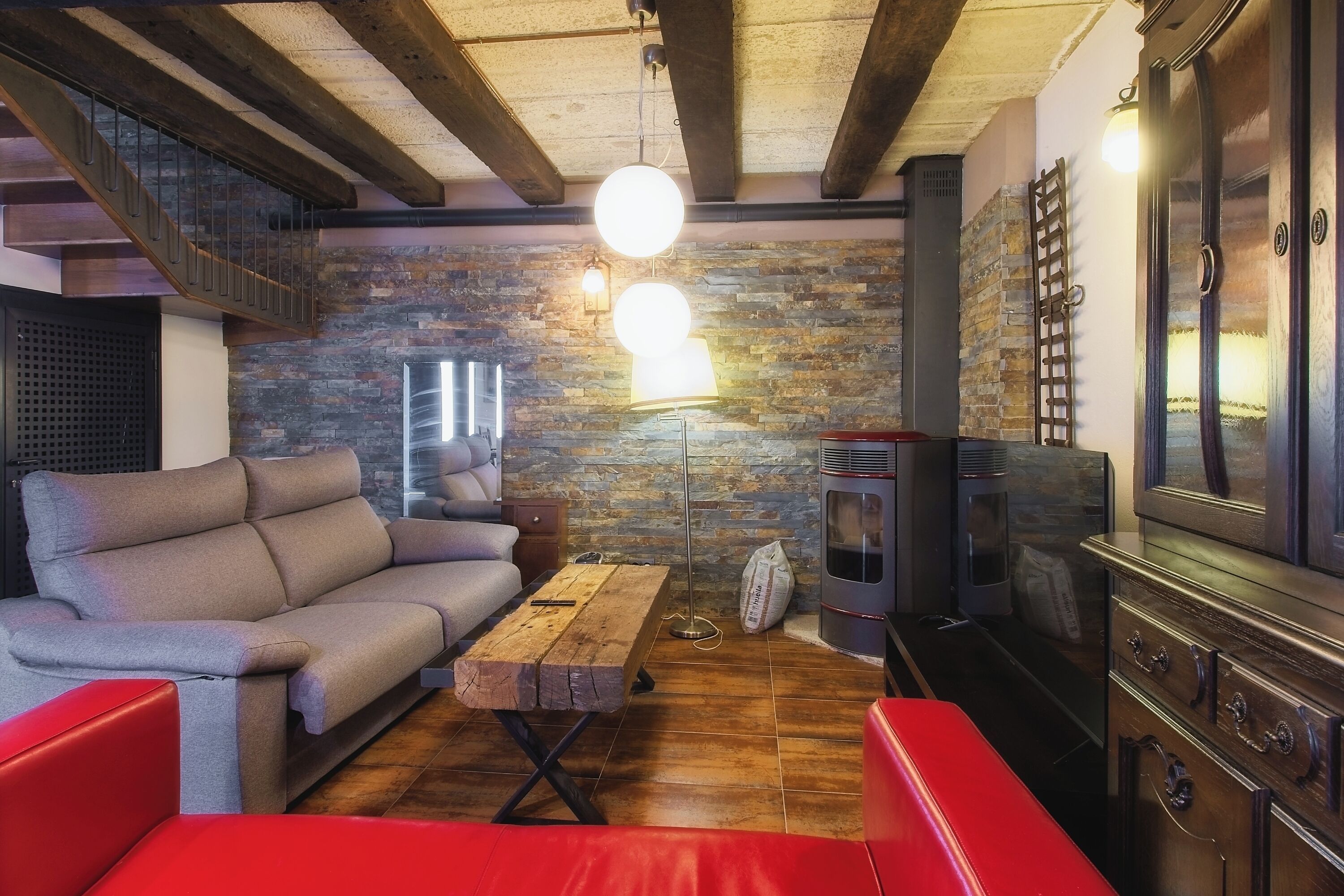 A cozy living room with a sofa, a wooden coffee table, a red bench, a fireplace, and a stone wall.