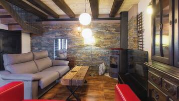 A cozy living room with a sofa, a wooden coffee table, a red bench, a fireplace, and a stone wall.