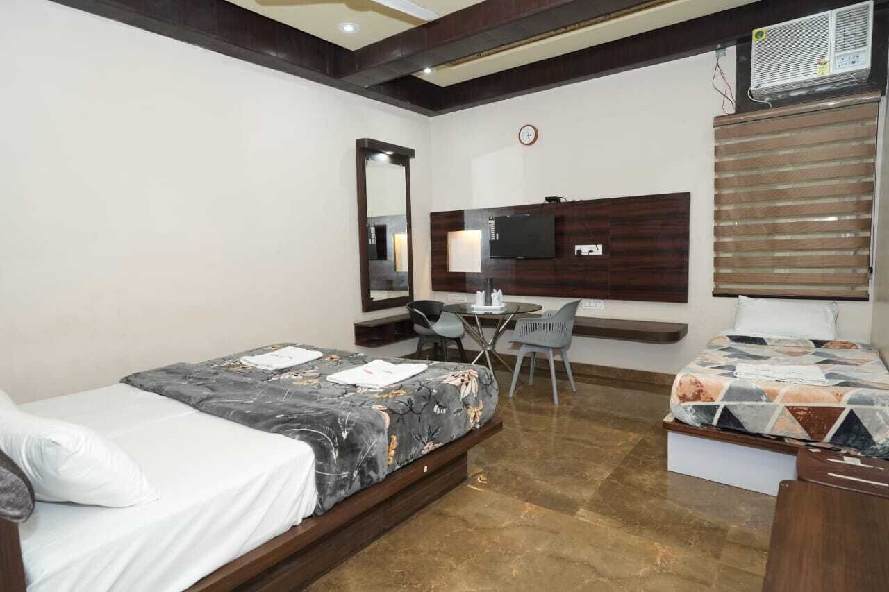 A hotel room with a bed, a desk with a chair, a TV, and a window with blinds.