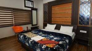 A bedroom with a large bed, a wooden headboard, a window with blinds, and a small orange chair. - Raj Mahal Hotel (Varanasi)