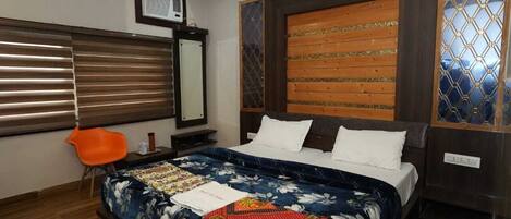 A bedroom with a large bed, a wooden headboard, a window with blinds, and a small orange chair.