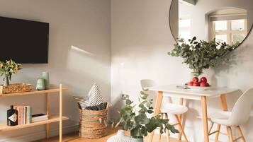 A modern living room with a flat-screen TV, a round mirror, a dining table with chairs, and a bookshelf.