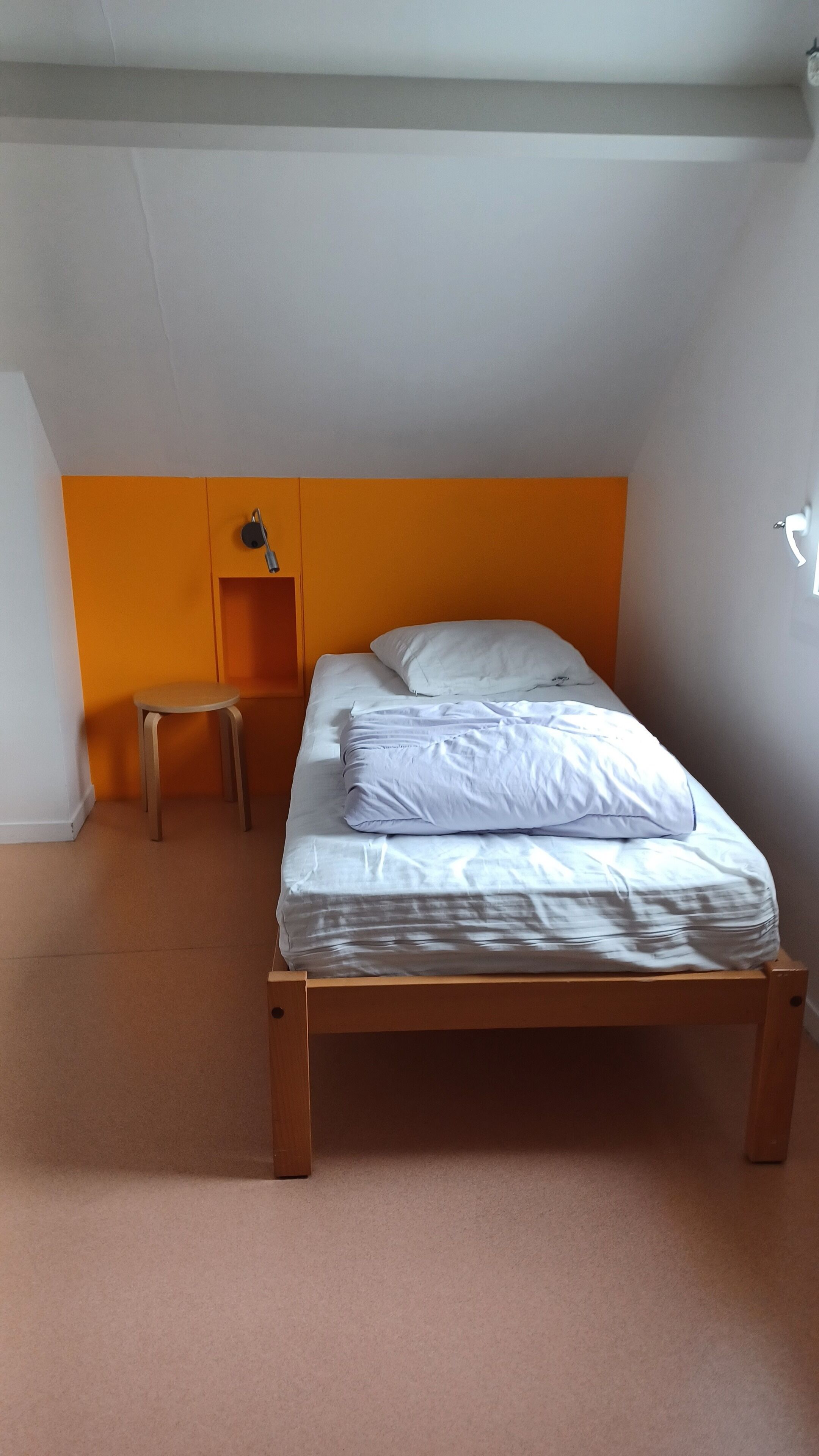 Ein Schlafzimmer mit einem Einzelbett, einem kleinen Hocker und einem Nachttisch.