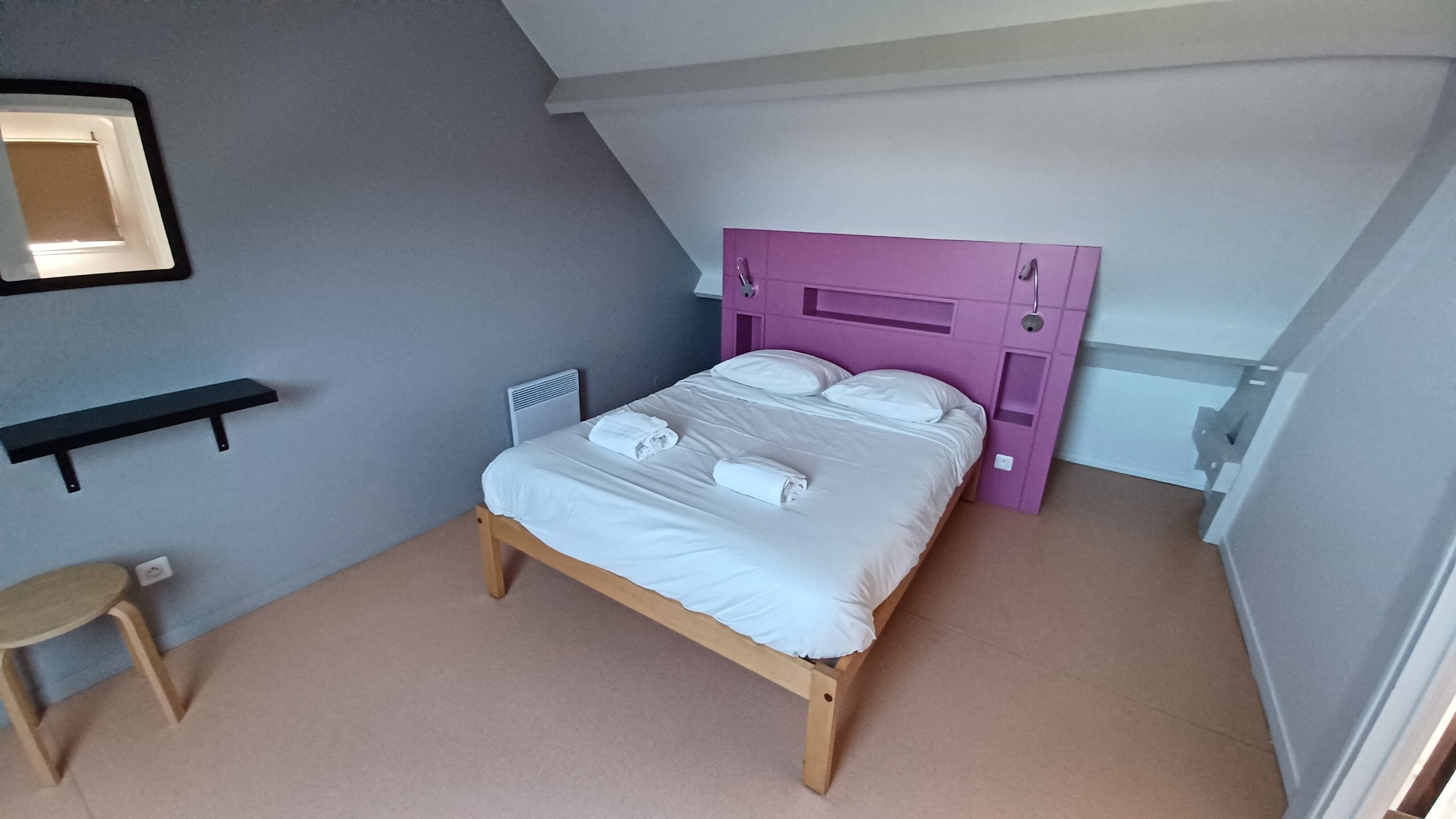 Une chambre à coucher avec un lit en bois, une tête de lit violette, une petite table de chevet et une chaise.