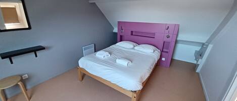 Une chambre à coucher avec un lit en bois, une tête de lit violette, une petite table de chevet et une chaise.