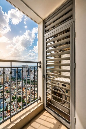 A balcony with a metal railing, a view of a cityscape, and a laundry room with stacked laundry baskets. - Vinhomes Skyline Apartment Saigon (Ho Chi Minh City)