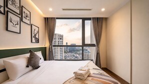 A hotel room with a large bed, a view of the city through a window, and framed artwork on the wall. - Vinhomes Skyline Apartment Saigon (Ho Chi Minh City)