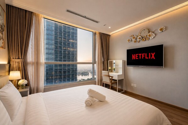 Habitación de hotel con una cama grande, un escritorio, un televisor mostrando 'NETFLIX' y vistas de un paisaje urbano a través de la ventana.