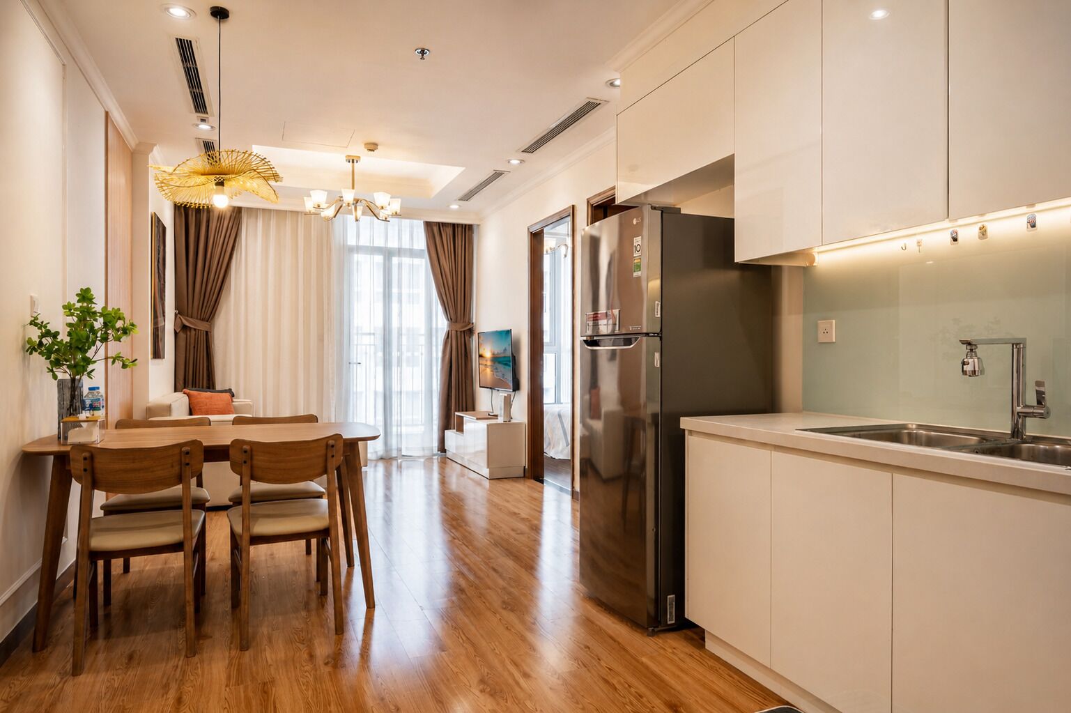 A modern kitchen with a stainless steel refrigerator, a dining area with wooden chairs and a table, and a large window with curtains.