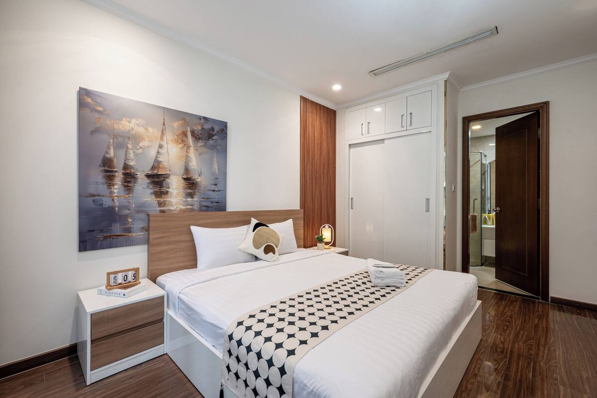 Habitación de hotel moderna con una cama grande, una mesita de noche, un armario y un cuadro en la pared.