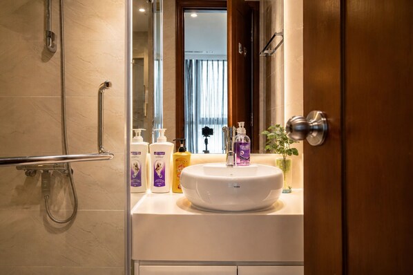 Een badkamer met een witte wastafel, een douchecabine van glas en toiletartikelen op het aanrecht.